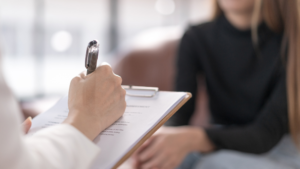 Close-up of a therapy session, showing a counselor writing on a clipboard while a patient sits across, symbolizing support and safe spaces for healing.