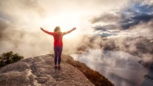 Person standing on a mountain with arms raised toward the sunrise, symbolizing clarity, purpose, and values-based leadership.